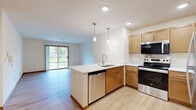 Located at 21025 George Hunt Circle in Waukesha, Wisconsin, this two-bedroom, two-bathroom single-floor residence offers a well-designed layout that balances comfort and functionality. The open-concept kitchen and living area serves as the heart of the home, where light hardwood-style flooring flows throughout. The kitchen is equipped with stainless steel appliances, warm wood cabinetry, a full suite of appliances including a refrigerator, range, and microwave, and a spacious peninsula with a white countertop and undermount sink, illuminated by elegant pendant lighting. The living room is bright and inviting, featuring a corner fireplace with a clean white surround, a ceiling fan, and multiple windows that invite natural light and outdoor views. The generously sized primary bedroom is carpeted and includes a ceiling fan with a window overlooking the exterior. The second bedroom also features carpet and hardwood-style flooring options. Two full bathrooms serve the unit — one with a soaking tub and vanity, the other with a walk-in shower, wood cabinetry, and built-in storage. A dedicated closet provides additional storage. Warm wood baseboards and trim details are consistent throughout, lending a cohesive and polished aesthetic to this well-appointed home.
