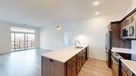 Located at 11130 N Buntrock Ave in Mequon, Wisconsin, this well-appointed two-bedroom, two-bathroom residence offers comfortable single-floor living with a clean, modern aesthetic. The open-concept layout connects the kitchen and living area seamlessly, creating an inviting and functional space. The kitchen is a standout feature, equipped with rich dark-stained cabinetry, crisp white quartz countertops, a herringbone tile backsplash, stainless steel appliances, and a central island with a built-in sink, illuminated by stylish pendant lighting. Light hardwood-style flooring flows throughout the main living areas, enhancing the bright, airy atmosphere. The spacious primary bedroom includes direct access to an en-suite bathroom and a generously sized walk-in closet with wire shelving. The second bedroom features plush carpet and a large window that invites natural light. Both bathrooms are finished with dark wood vanities, white countertops, and tiled tub-shower combinations with large mirrors. A dedicated laundry room houses a full-size washer and dryer. Two closets provide ample storage throughout. The overall design is contemporary and cohesive, with a neutral palette and quality finishes that make this residence a polished and practical home.