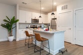 This single-story unit in Advance, NC offers a thoughtfully designed layout across a comfortable footprint. The open-concept living room features light wood-look flooring, a ceiling fan, and a large window that invites natural light, creating a bright and airy atmosphere. The adjacent kitchen is well-equipped with white shaker cabinetry, granite countertops, stainless steel appliances, a subway tile backsplash, and a central island with seating for two, finished with stylish pendant lighting overhead.

The primary bedroom features plush carpeting, a ceiling fan, and a generously sized walk-in closet outfitted with wire shelving systems. The primary bathroom includes a double-sink vanity with granite countertops, white cabinetry, and wood-look flooring. An additional full bathroom features a tub-shower combination with brushed nickel fixtures. A dedicated office provides carpeted flooring and a bright window, offering a functional workspace. Two closets throughout the unit provide ample storage. The overall aesthetic is clean and modern, with a neutral palette and consistent finishes throughout.
