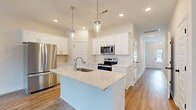 This two-story home showcases a clean, contemporary design with a neutral color palette and light hardwood-style flooring that runs consistently throughout both levels, creating a cohesive and airy feel.

The kitchen serves as a central highlight of the main floor, featuring white shaker cabinetry, crisp white quartz countertops, and a large center island with an integrated sink. Stainless steel appliances, including a refrigerator, range, and microwave, complement the space, while pendant lighting with glass fixtures adds a refined touch overhead.

Adjacent to the kitchen, the dining area benefits from natural light through multiple windows and a glass-panel door, with a chandelier providing an elegant focal point. The living area continues the open, light-filled atmosphere, complete with a ceiling fan and additional access to the outdoors.

A staircase with wood-tread steps and white risers connects the two floors, leading to the upper level where the bedrooms are located. These rooms feature vaulted ceilings, ceiling fans, and windows that frame outdoor views. The upper-level bathroom offers a long double-vanity with white cabinetry, quartz countertops, and a separate water closet, while a compact half bath is also available on the main floor.