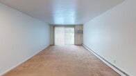 Located at 100 S Village Blvd in Baldwinsville, NY, this one-bedroom, one-bathroom apartment offers a functional and straightforward layout across a single floor. The combined kitchen and living area forms the heart of the unit. The living room is carpeted and features large sliding glass doors with vertical blinds, filling the space with natural light and providing outdoor views. A wall-mounted air conditioning unit and baseboard heating ensure year-round comfort. The kitchen is efficiently designed with warm wood-toned cabinetry, white countertops, and wood-look vinyl flooring. It is equipped with a electric coil range, under-cabinet range hood, dishwasher, and a single-basin stainless steel sink, providing ample functionality for everyday cooking. A hallway connects the main living area to the private bedroom, which is generously sized and features plush carpeting, a window with natural light, and baseboard heating. A dedicated closet provides convenient storage. The bathroom is clean and practical, featuring wood-toned cabinetry with a vanity sink, a mirrored medicine cabinet, tiled flooring, and overhead vanity lighting. Neutral tones and white walls throughout the unit create a bright, move-in-ready atmosphere.