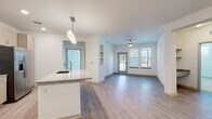 This well-appointed single-floor residence showcases a thoughtfully designed open-concept layout that seamlessly connects the kitchen and living areas. The kitchen is a standout feature, equipped with stainless steel appliances — including a range, over-the-range microwave, and a French door refrigerator — complemented by light wood-toned cabinetry, a subway tile backsplash, and granite countertops. A large central island with a built-in sink and a modern pendant light fixture serves as both a functional workspace and a natural gathering point.

The living area flows directly from the kitchen, featuring durable wood-look flooring, a ceiling fan, built-in shelving niches, and a glass-paned door that invites natural light from adjacent windows, creating a bright and open ambiance.

The bedrooms offer plush carpeting, generous natural light through multiple windows with blinds, and ceiling fans for year-round comfort. The bathrooms are finished with granite-topped vanities and wood-look tile flooring. The primary bathroom features a glass-enclosed shower, while a secondary bath offers a full tub-shower combination with elegant stone-look tile surround. Clean white walls and consistent modern finishes give the entire space a cohesive, contemporary feel.
