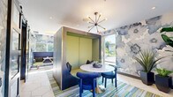 Located at 155 Ames St in Marlborough, Massachusetts, this thoughtfully designed lounge space makes a striking first impression with its immersive, large-scale watercolor floral wall murals in shades of blue, white, and grey that wrap the room in artistic energy. The single-floor layout is efficiently organized into distinct functional zones that encourage both collaboration and casual gathering.

At the heart of the space sits a central enclosed booth — a sleek, steel-framed cube with a sage green interior — paired with a round marble-top table and deep blue upholstered chairs, all anchored by a multicolored striped area rug and illuminated by a mid-century modern sputnik chandelier overhead. Large glass panels and floor-to-ceiling windows allow generous natural light to pour in, offering views of the surrounding greenery.

A secondary seating nook features high-backed navy blue acoustic panels that create a semi-private work area with built-in power access, ideal for focused tasks. A lounge area with a marble-top communal table and a glowing neon "Think Outside The Box" sign adds a motivational and modern touch. Large-format white hexagonal tile flooring ties the entire space together with a clean, contemporary aesthetic. Lush potted plants add warmth and life throughout.