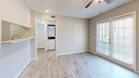 This single-story unit offers a clean, neutral aesthetic throughout, with light-toned walls and white trim creating a bright, cohesive feel. The main living area features light wood-look vinyl flooring, a ceiling fan, and a front entry door with a textured ceiling overhead. Natural light filters in through window treatments, enhancing the open feel of the space.

The galley-style kitchen is efficiently laid out, featuring white cabinetry, light countertops, a stainless steel double-basin sink, and a full suite of stainless steel appliances including a refrigerator, gas range, and dishwasher. Light wood-look flooring continues throughout this area.

A dedicated area accommodates a stacked washer and dryer unit, conveniently accessible alongside a closet with louvered doors. The bedrooms are carpeted and receive ample natural light through sizable windows fitted with blinds; each room includes a ceiling fan and features neutral gray-toned walls.

The bathroom is finished with white tile surrounding a full tub-shower combination, complemented by chrome fixtures and a clean, minimal design. Overall, the space presents a functional, well-maintained interior with consistent finishes throughout.
