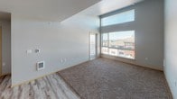 Located at 21815 29th Ave S in Des Moines, Washington, this single-floor unit is situated on an upper level, offering notable views of the surrounding neighborhood and what appears to be distant water or horizon scenery. The layout is thoughtfully organized, with distinct living, kitchen, and bedroom areas interconnected by an efficient floor plan.

The kitchen serves as a functional centerpiece, featuring stainless steel appliances including a refrigerator, range, and over-the-range microwave. Contemporary wood-toned cabinetry provides generous storage, while a central island with a light stone-finish countertop offers additional workspace and casual seating potential. Light hardwood-style flooring runs throughout the kitchen and entry areas, lending warmth and easy maintenance.

The living area is generously proportioned, with soaring ceilings that amplify the sense of space. Large windows, including an elevated clerestory-style window, flood the room with natural light and frame views of the surrounding area. A sliding glass door provides direct access to a private balcony. Plush carpet covers the living room floor, adding comfort underfoot.

Multiple bedrooms feature neutral carpet, soft gray walls, and blinds-covered windows. The primary bedroom benefits from dual windows capturing expansive outdoor views. Additional bedrooms offer a quieter setting with single windows. The overall aesthetic is clean, modern, and move-in ready.