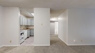 This single-floor, 3-bedroom, 1-bathroom unit offers a straightforward and functional layout designed for comfortable everyday living. The open-concept area connects the kitchen and living room, creating a cohesive shared space. The kitchen features gray cabinetry, a countertop sink, a white range, and a dishwasher, with durable flooring that transitions into the carpeted living area. A textured ceiling is present throughout the main living spaces, adding a subtle design detail overhead.

The three bedrooms are each carpeted and finished in neutral tones, providing a calm and versatile backdrop. The spacious primary bedroom includes a window with outdoor views and a baseboard heater, while the additional bedrooms feature sliding-door closets, windows for natural light, and baseboard heating as well. Multiple hallways connect the rooms, ensuring an organized flow throughout the unit.

The full bathroom is well-appointed with a tiled tub-and-shower combination, a wood-toned vanity with a granite-style countertop, a large mirror, and neutral tile flooring. A wall-mounted heater and thermostat are also present, reflecting practical climate control throughout the unit. Overall, the space presents a clean, move-in-ready environment with consistent neutral finishes.