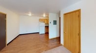 This single-floor unit offers a practical and straightforward layout with a cohesive neutral palette throughout. The entry area transitions between soft carpet and warm hardwood-style flooring, providing a clear visual separation between the living space and the kitchen zone. The living area is open and well-proportioned, featuring a textured popcorn ceiling, flush-mount lighting, and a baseboard heating unit along the wall. Natural light filters in through a window near the entry, keeping the space bright and welcoming.

The kitchen is efficiently designed with warm oak cabinetry extending to the upper walls, dark granite-style countertops, a stainless steel sink, and white appliances including a refrigerator, electric range, and an overhead ventilation hood. The hardwood-style flooring continues throughout the kitchen, adding warmth and easy maintenance.

The bedroom is carpeted and quiet, with white walls, wood-trimmed baseboards, and a window that allows natural light. The textured ceiling and flush-mount fixture maintain consistency with the rest of the unit.

The bathroom is clean and functional, featuring a wood-framed vanity mirror, a single-basin sink with oak cabinetry below, a full-size soaking tub with a shower, and chrome fixtures throughout. The overall ambiance of the unit is simple, neutral, and move-in ready.