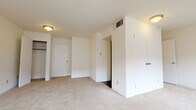 This single-floor residence offers a clean, functional layout designed to maximize usable space throughout. The living area is generously sized, finished with plush light-colored carpeting and crisp white walls that create a bright, open atmosphere. Multiple windows fitted with blinds allow natural light to filter in while offering views of the surrounding exterior.

The bedroom is well-proportioned, also carpeted, and features multiple closet options, including what appears to be a walk-in and an additional standard closet, providing substantial storage capacity. An entry door leads directly into this space, adding a practical layout element.

The galley-style kitchen contrasts the lighter living areas with rich, dark wood cabinetry and dark countertops. It is equipped with a stainless steel range, black refrigerator, dishwasher, and a stainless steel sink, offering a full suite of appliances along dark hardwood-style flooring.

The bathroom continues the dark hardwood-style flooring and features a rich wood vanity with a white countertop, a full-sized soaking tub with a classic square tile surround, and a chrome fixtures throughout, contributing a clean and functional aesthetic to the space.