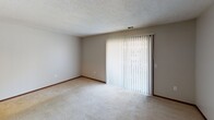 This single-floor residence in West Middlesex, Pennsylvania offers a practical and comfortable layout designed for easy everyday living. The floor plan, as seen in the overhead view, reveals a well-organized arrangement of living, sleeping, kitchen, and bathroom spaces flowing cohesively throughout the home.

The living area is generously proportioned, featuring light-toned carpeting, neutral wall tones, and a textured ceiling. A large sliding glass door dressed with vertical blinds allows natural light to fill the space and provides access to the outdoors. An adjacent area with warm hardwood-style flooring adds visual variety and connects the living space to the rest of the home.

The kitchen is equipped with warm oak cabinetry offering ample storage, dark laminate countertops, a double stainless steel sink, and a black electric range with an overhead ventilation hood — a functional setup suited for everyday cooking.

The bedrooms are carpeted and well-lit, with windows dressed in blinds that bring in natural light. One bedroom features a walk-in closet outfitted with double hanging rods and shelving, providing generous storage capacity. Another bedroom includes a dedicated closet with built-in shelving.

The bathrooms include a full bath with a soaking tub and tiled surround featuring built-in niches, as well as a secondary bathroom with hardwood-style flooring. Throughout the home, dark wood trim provides a consistent finishing detail.