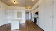 Located on Milwaukee's vibrant East Side at 1840 N Farwell Ave, this thoughtfully designed studio unit blends industrial aesthetics with modern finishes. The exposed concrete ceiling serves as a defining architectural element throughout, complementing the rich hardwood-style flooring that runs continuously across the open-plan living space.

The kitchen is well-appointed with white shaker-style cabinetry extending floor to ceiling, granite countertops, a classic subway tile backsplash, and a full suite of stainless steel appliances including a range, over-the-range microwave, dishwasher, and refrigerator. Ample cabinet storage ensures excellent organization within the compact footprint.

The living area incorporates a built-in Murphy bed system with integrated shelving and a fold-down desk, maximizing functionality without sacrificing space. A wall of tall white built-in wardrobes provides generous clothing and storage solutions adjacent to sliding glass doors that open to a private balcony offering sweeping views of the Milwaukee skyline and surrounding neighborhood.

The bathroom features warm wood-tone flooring, a walk-in shower with a clean white surround, and a contemporary door with a wood-grain finish. Throughout the unit, a neutral, light-filled palette and clean-lined modern design create a cohesive and comfortable urban living environment.