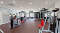 Located at Kensington Circle in Wheaton, Illinois, this well-appointed fitness center is designed to support a comprehensive workout experience across its single-floor layout. The facility is divided into distinct functional zones, each thoughtfully equipped for a variety of training styles.

The cardio area houses a row of Matrix treadmills and elliptical machines arranged beneath vaulted ceilings with recessed lighting and ceiling fans for air circulation. A striking arched window floods this section with natural light and offers views of the surrounding outdoor area, including a community pool.

The strength training zone is generously outfitted with a wide selection of Matrix selectorized machines featuring red upholstery, a multi-functional cable station, and a dedicated free weight area with a full dumbbell rack and adjustable benches. Large windows along the accent-painted charcoal walls bring in additional daylight and provide views of the pool and landscaped grounds.

A separate room accessed via glass-panel doors offers additional machine stations and mirrors, enhancing the sense of space. Throughout the facility, durable rubber flooring in a dark speckled finish provides safety and comfort underfoot. The overall design balances a modern, energetic aesthetic with a practical, user-focused layout.