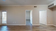 This single-floor unit offers a clean, modern design characterized by warm neutral tones, wood-look flooring throughout, and crisp white trim and crown molding that lend a polished, cohesive aesthetic. The open-concept living and dining area flows seamlessly into the kitchen, which is outfitted with stainless steel appliances — including a range, microwave, and dishwasher — white shaker-style cabinetry with brushed nickel hardware, a gray countertop, and a classic subway tile backsplash. A peninsula counter provides additional workspace and a natural division between the kitchen and living area. The living space is bright and welcoming, with a ceiling fan and large window that invites natural light. The bedroom continues the warm flooring and neutral palette, featuring a generous window with exterior views and a ceiling fan for added comfort. A full bathroom includes a tub-shower combination, providing functional simplicity. Additional storage is accessible via a spacious closet. The layout, as seen in the dollhouse view, is efficiently organized, with clear separation between the living, sleeping, and bathroom areas. Overall, the unit presents a fresh, move-in-ready environment that balances practicality with contemporary residential design.