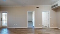 This single-floor unit offers a clean, modern design characterized by warm neutral tones, wood-look flooring throughout, and crisp white trim and crown molding that lend a polished, cohesive aesthetic. The open-concept living and dining area flows seamlessly into the kitchen, which is outfitted with stainless steel appliances — including a range, microwave, and dishwasher — white shaker-style cabinetry with brushed nickel hardware, a gray countertop, and a classic subway tile backsplash. A peninsula counter provides additional workspace and a natural division between the kitchen and living area. The living space is bright and welcoming, with a ceiling fan and large window that invites natural light. The bedroom continues the warm flooring and neutral palette, featuring a generous window with exterior views and a ceiling fan for added comfort. A full bathroom includes a tub-shower combination, providing functional simplicity. Additional storage is accessible via a spacious closet. The layout, as seen in the dollhouse view, is efficiently organized, with clear separation between the living, sleeping, and bathroom areas. Overall, the unit presents a fresh, move-in-ready environment that balances practicality with contemporary residential design.