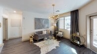 This single-floor residence showcases a cohesive contemporary design with glamorous accents throughout. The living area serves as the focal point, featuring dark hardwood-style flooring, a striking sputnik chandelier with gold and crystal detailing, and floor-to-ceiling charcoal drapes that frame windows offering outdoor views of surrounding greenery. A neutral cowhide rug and glass-topped gold coffee table anchor the seating arrangement, while abstract wall art adds a sophisticated touch.

The kitchen is outfitted with tall white shaker cabinetry, granite countertops, a white subway tile backsplash, and stainless steel appliances. A peninsula island with pendant lighting provides additional seating and prep space.

The primary bedroom features a tufted upholstered headboard, ceiling fan, and large windows with coordinating drapes. An additional bedroom offers carpeted flooring and a decorative gallery wall of hexagonal mirrors with warm gold accents.

Two bathrooms serve the residence. The primary bath includes an elongated vanity with granite counters, an LED-backlit mirror, wood-look flooring, and access to a walk-in closet. The secondary bathroom features a glass-enclosed walk-in shower with white tile surround and brushed nickel fixtures. The overall ambiance is modern and polished with a warm, curated aesthetic.