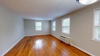 Located at 2603 Eighth St S in Arlington, VA, this one-bedroom, one-bathroom unit offers a well-organized single-level layout across a comfortable living footprint. Rich, warm-toned hardwood floors flow consistently throughout the living room, bedroom, and hallways, lending the space a classic and cohesive character.

The living room is generously proportioned, with multiple windows that invite natural light and offer views of surrounding greenery. A wall-mounted HVAC unit and a pendant light fixture add functional detail to the space. The bedroom is comfortably sized, featuring two windows with blinds that provide both natural light and privacy, along with its own wall HVAC unit.

The kitchen is distinct in its finishes, transitioning to clean marble-look tile flooring. It features rich wood cabinetry, light granite-style countertops, a stainless steel sink, and a black electric range with overhead ventilation. A window above the counter keeps the kitchen bright.

The bathroom is neatly appointed with a wood vanity, white countertop, mirror, and vanity lighting. Two connecting hallways provide smooth circulation between all rooms. Neutral gray walls throughout the unit create a clean, versatile backdrop well-suited to a variety of interior styles.