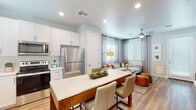 This single-floor residence offers a thoughtfully designed open-concept layout that seamlessly connects the kitchen, dining, and living areas. The kitchen is outfitted with white shaker-style cabinetry extending to the ceiling, light quartz countertops, and a full suite of stainless steel appliances including a range, microwave, dishwasher, and refrigerator. A wood-based kitchen island with a quartz top provides additional prep space and casual seating for multiple guests. Recessed lighting and a window above the sink keep the kitchen bright and functional.

The living area extends naturally from the kitchen and dining space, featuring large windows dressed with blinds and curtain panels that allow ample natural light. A ceiling fan adds comfort to the space. Light wood-style flooring runs consistently throughout the unit, adding warmth and visual continuity.

The two bedrooms are comfortably sized, each featuring a ceiling fan, large windows with blinds and drape panels, and the same wood-style flooring. The bathroom is finished with white cabinetry, a quartz vanity countertop, a glass-enclosed shower, and modern fixtures, maintaining the clean, contemporary aesthetic found throughout the space.