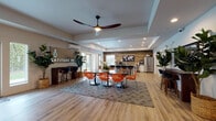 The Latitude 45 clubhouse at 2001 NE 112th Ave in Vancouver, Washington, is a thoughtfully designed single-floor community space that seamlessly blends comfort, functionality, and modern style. Upon entry, residents and guests are welcomed by a bright, open foyer featuring light hardwood-style flooring, a striking Latitude 45 branded sign, and a tall fiddle-leaf fig tree that adds a natural touch. Large windows and glass-paneled entry doors flood the space with natural light and offer views of the surrounding greenery.

The open-plan layout connects several distinct areas in one expansive, airy environment. A welcoming lounge area features plush seating, a wall-mounted flat-screen television, and elegant ceiling fans that underscore the room's generous ceiling height. Tray ceiling details add architectural interest throughout the space.

The dining area showcases a round pedestal table surrounded by vibrant orange lattice-back chairs, creating a bold, energetic focal point at the heart of the room. Adjacent to it, a well-appointed kitchen features a large central island with bar seating, white cabinetry, quartz countertops, stainless steel appliances, and a dramatic wood-planked accent wall. A separate bar-height counter near the entry provides additional workspace or casual seating. A flex area with bright orange accent chairs offers additional gathering space, with access to a private office or meeting room through glass-paneled French doors.