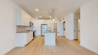 Located at 10421 Daybreak Trail Ct in Sun City Center, Florida, this single-story residence showcases a clean, contemporary design with a bright and airy aesthetic throughout. The open-concept layout is anchored by a well-appointed kitchen featuring crisp white cabinetry extending to the ceiling, granite countertops, and a full suite of stainless steel appliances including a refrigerator, range, and over-the-range microwave. A central island with an undermount sink and bronze-finish pull-down faucet serves as both a functional workspace and a visual focal point, illuminated by stylish globe pendant lights overhead. Light-toned wood flooring flows seamlessly through the main living areas, enhancing the sense of openness and continuity.

The living area benefits from natural light through a sliding glass door that opens to an outdoor balcony, complemented by a ceiling fan for year-round comfort. Bedrooms offer plush carpeting and ample natural light via large windows with views of the surrounding community. The bathroom is finished with granite vanity counters, matching bronze hardware, light wood-look flooring, and a tiled soaking tub-shower combination. A dedicated laundry area with stacked units is also included, adding practical convenience to this thoughtfully designed home.