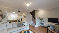 This three-story residence is thoughtfully designed with a cohesive blend of modern and transitional style throughout. The main living area features warm hardwood-style flooring, crown molding, and a staircase with classic white newel posts, creating an inviting atmosphere. A ceiling fan provides comfort, while the open layout connects seamlessly to the dining area beyond.

Two distinct kitchen spaces are present within the home. Both feature a striking two-tone design with charcoal lower cabinetry, white upper cabinets, white subway tile backsplashes, light countertops, and stainless steel appliances. One kitchen opens directly to a living space with sliding glass doors that allow abundant natural light and outdoor views.

The living room is a bright, relaxed space anchored by a large sectional sofa, a natural wood coffee table, and sliding glass doors that open to an exterior area. Bedrooms are generously sized with hardwood-style flooring, ceiling fans, and access to closets. One bedroom features an en-suite bathroom, while additional bathrooms offer tiled shower enclosures and dark vanity cabinetry with light countertops. A dedicated in-unit laundry area with a full-size washer and dryer adds everyday convenience throughout this well-finished home.