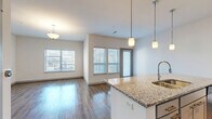 Located at 601 Avenida Cesar E Chavez in Kansas City, MO, this well-appointed one-bedroom, one-bathroom residence offers a thoughtfully designed layout across a single floor. The open-concept living space seamlessly integrates the kitchen, dining, and living areas, creating a bright and airy atmosphere filled with natural light from multiple large windows. The kitchen is a standout feature, showcasing a granite-topped island with pendant lighting, white cabinetry, stainless steel appliances including a refrigerator, microwave, and range, and a classic subway tile backsplash — all set above durable wood-style flooring. The living and dining area extends toward a private balcony, accessible through a glass door, ideal for enjoying outdoor views. The bedroom offers plush carpeting, a ceiling fan, and a bright window, complemented by two generously sized closets with wire shelving systems for ample storage. The full bathroom features granite countertops, gray cabinetry, a soaking tub with tiled surround, and wood-style flooring. A dedicated laundry area with a stacked washer and dryer adds everyday convenience. A utility room rounds out this efficiently designed and modern residence.