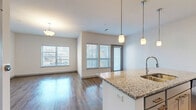 Located at 601 Avenida Cesar E Chavez in Kansas City, MO, this well-appointed one-bedroom, one-bathroom residence offers a thoughtfully designed layout across a single floor. The open-concept living space seamlessly integrates the kitchen, dining, and living areas, creating a bright and airy atmosphere filled with natural light from multiple large windows. The kitchen is a standout feature, showcasing a granite-topped island with pendant lighting, white cabinetry, stainless steel appliances including a refrigerator, microwave, and range, and a classic subway tile backsplash — all set above durable wood-style flooring. The living and dining area extends toward a private balcony, accessible through a glass door, ideal for enjoying outdoor views. The bedroom offers plush carpeting, a ceiling fan, and a bright window, complemented by two generously sized closets with wire shelving systems for ample storage. The full bathroom features granite countertops, gray cabinetry, a soaking tub with tiled surround, and wood-style flooring. A dedicated laundry area with a stacked washer and dryer adds everyday convenience. A utility room rounds out this efficiently designed and modern residence.