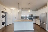 Located at 455 S Maple Avenue in Falls Church, VA, this well-appointed 2-bedroom, 2-bathroom residence offers a thoughtfully designed single-level layout. The open-concept living and dining area is anchored by rich dark hardwood flooring and large windows that invite abundant natural light and outdoor views. The modern kitchen serves as the centerpiece of the home, featuring a large granite-topped island with pendant lighting, crisp white cabinetry, a gray subway tile backsplash, and a full suite of stainless steel appliances including a range, microwave, and refrigerator. Track lighting complements the pendant fixtures overhead. Both bedrooms are carpeted and well-lit with windows overlooking greenery, offering a calm and comfortable retreat. Three closets, including a walk-in closet in the primary suite, provide ample storage. The two bathrooms are finished with granite-topped vanities, dark wood cabinetry, and tile flooring; the second bath includes a tub-shower combination with subway tile surround. Additional conveniences include an in-unit laundry and a private patio, rounding out this modern and functional residence.