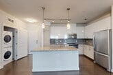 Located at 455 S Maple Avenue in Falls Church, VA, this well-appointed 2-bedroom, 2-bathroom residence offers a thoughtfully designed single-level layout. The open-concept living and dining area is anchored by rich dark hardwood flooring and large windows that invite abundant natural light and outdoor views. The modern kitchen serves as the centerpiece of the home, featuring a large granite-topped island with pendant lighting, crisp white cabinetry, a gray subway tile backsplash, and a full suite of stainless steel appliances including a range, microwave, and refrigerator. Track lighting complements the pendant fixtures overhead. Both bedrooms are carpeted and well-lit with windows overlooking greenery, offering a calm and comfortable retreat. Three closets, including a walk-in closet in the primary suite, provide ample storage. The two bathrooms are finished with granite-topped vanities, dark wood cabinetry, and tile flooring; the second bath includes a tub-shower combination with subway tile surround. Additional conveniences include an in-unit laundry and a private patio, rounding out this modern and functional residence.