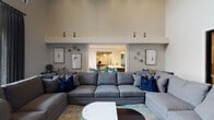 Located at 301 22nd Ave N in Nashville, TN, this single-floor amenity space offers a sophisticated and thoughtfully designed environment built for socializing and entertainment. The open-concept layout connects several distinct zones seamlessly, creating a fluid and inviting atmosphere throughout.

The central lounge area is anchored by a generously sized sectional sofa in warm gray upholstery, accented with navy and teal throw pillows. Soaring ceilings lend the space a grand, airy quality, while recessed lighting and decorative pendant fixtures provide layered illumination. Curated artwork and decorative wall accents contribute to the polished aesthetic.

Adjacent to the lounge is a well-appointed wet bar and kitchenette area, featuring a large white quartz island with bar seating, dark cabinetry, under-counter appliances, and a mounted flat-screen television set against a striking herringbone tile backsplash framed by textured accent tile. Vibrant teal abstract art panels add bold color to the space.

A dedicated game room is visible through an open passageway, housing a full-size pool table set on patterned carpet beneath pendant lighting, making it ideal for recreation and casual gatherings. The overall design palette — neutral tones with teal, navy, and gold accents — creates a contemporary yet welcoming ambiance throughout the entire space.