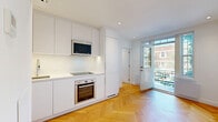 Located at 590 Avenue Outremont in the desirable Outremont neighbourhood of Montréal, this thoughtfully designed one-bedroom, one-bathroom unit makes efficient use of its compact footprint across a single floor. Throughout the living areas and bedroom, warm herringbone-patterned hardwood flooring adds a timeless, elegant touch that contrasts beautifully with the crisp white walls.

The kitchen is outfitted with sleek, flat-front white cabinetry extending from counter to ceiling, maximizing storage. Stainless steel appliances — including a built-in oven, induction cooktop, and over-the-range microwave — complement the clean white countertops for a polished, modern aesthetic.

The living area benefits from a large window and glass door that opens to a small balcony, allowing natural light to fill the space and offering pleasant green views of the surrounding trees.

The bedroom is cozy and functional, with herringbone floors continuing throughout and a frosted glass window providing privacy while still admitting natural light.

The bathroom features a contemporary design with large-format neutral tiles, a wall-mounted floating vanity, and a glass-enclosed walk-in shower, creating a clean and spa-like atmosphere. Grab bars are thoughtfully integrated, adding accessibility to the refined design.