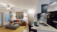 This 2-bedroom, 1-bathroom single-story residence features an open-concept layout that connects the living, dining, and kitchen areas into one cohesive, functional space. Wood-style flooring runs throughout the main living areas, complementing the bright white walls and creating a clean, modern aesthetic.

The kitchen is designed in a galley style, featuring bold black cabinetry, granite countertops, a tile backsplash, and black appliances including a refrigerator, range, and microwave. A peninsula with a granite surface and sink extends into the living area, providing additional prep space and casual seating. A dedicated dining area sits adjacent to the kitchen, offering a natural separation within the open floor plan.

The living room is spacious and well-lit, with a ceiling fan and sliding glass doors that allow natural light to fill the room. Both bedrooms offer plush carpeting, ceiling fans, and ample wall space. One bedroom features vaulted-style ceilings, adding an airy feel to the room, while both include windows that bring in natural light.

The shared bathroom includes dark cabinetry, granite countertops, a large mirror, and wood-style flooring. A utility area with washer/dryer connections is accessible through the kitchen.