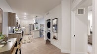 Located at 8355 E 32nd Ave in Denver's vibrant Central Park neighborhood, this well-appointed one-bedroom, one-bathroom residence offers a thoughtfully designed single-floor layout with modern finishes throughout. Light wood-tone flooring flows seamlessly across the main living areas, creating a cohesive and airy aesthetic.

The kitchen is a standout feature, showcasing flat-front cabinetry in a warm wood finish, a full suite of stainless steel appliances including a gas range and French door refrigerator, a tiled backsplash, and a central island with bar seating illuminated by striking black pendant lights — ideal for casual dining and entertaining.

The open-concept living room is bright and welcoming, benefiting from large windows and a glass door that invite natural light and provide access to an outdoor balcony with neighborhood views. The bedroom offers a comfortable retreat with carpet flooring, generous natural light, a dedicated closet, and direct access to the bathroom.

The bathroom features a dual-sink vanity with light wood cabinetry, dark hardware accents, a quartz countertop, and a large mirror — combining style with practicality. A dedicated in-unit laundry closet with a stacked washer and dryer adds everyday convenience. The overall design balances contemporary style with functional living.