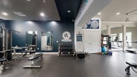 The Athletic Club at Florin Hill, located at 104 Merchant Ave in Mount Joy, PA, is a thoughtfully designed fitness facility that offers a comprehensive workout environment across a single, open floor. The space is divided into distinct functional zones, each catering to different aspects of physical training.

The cardio area features a row of modern treadmills and elliptical machines positioned facing large windows and glass double doors, flooding the space with natural light and providing views of the surrounding greenery. Track lighting runs along the ceiling, complementing the bright, open atmosphere.

Adjacent to the cardio zone, the strength training area is anchored by a full rack of dumbbells, a weight bench, and mirrored walls that visually expand the space. Bold navy-blue accent walls branded with the Athletic Club at Florin Hill logo add a strong, motivating aesthetic. Inspirational wall text reading "I Like to Move It / MOVE IT" reinforces the energetic ambiance throughout.

A functional training section offers stability balls, kettlebells, resistance bands, and yoga mats neatly organized on shelving units, supporting a wide variety of workout modalities. The durable rubber flooring throughout provides safety and comfort underfoot.

Crown molding and clean white architectural columns lend a refined, polished character to the space, balancing its athletic purpose with a welcoming, upscale feel.