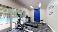 The ONE30 Cole fitness center, located at 130 Cole Manor Drive in Athens, Georgia, is a purpose-built exercise facility designed to support an active lifestyle. The single-floor space features a clean, modern aesthetic defined by white-painted concrete block walls accented by a bold royal blue panel — a color that also runs through the geometric-patterned carpet tiles underfoot, tying the room together with a cohesive, energetic look.

The room is equipped with a well-rounded selection of Spirit-brand cardio machines, including a treadmill, elliptical, and rowing machine, all featuring digital display consoles. A rack of dumbbells provides options for strength training, while a dedicated accessory station holds resistance bands, medicine balls, stability balls, and foam rollers to support flexibility and functional fitness routines.

Large windows and a glass-paneled door line one wall, flooding the space with natural light and offering direct views of the adjacent outdoor pool and surrounding tree line — creating an open, inviting atmosphere. Recessed fluorescent lighting supplements natural light overhead.

A glass door leads directly to the pool area, making it easy to transition between indoor workouts and outdoor amenities. The space is branded with the "ONE30 Cole" name prominently displayed on the wall, reinforcing its identity as a dedicated community fitness amenity.