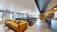 Located at 2650 University Ave SE in Minneapolis, MN, this generously sized amenity floor offers a thoughtfully designed collection of social and recreational spaces within a contemporary mixed-use building. The exterior showcases a classic dark brick façade with large gridded windows and well-maintained landscaping, lending the building a polished, modern character.

Inside, the main lounge area is an open, light-filled space with polished concrete floors, bold statement lighting featuring globe pendant clusters, and a vibrant large-scale botanical mural that serves as a striking focal point. A billiards table anchors the game area, while modular seating in warm mustard tones invites relaxed gatherings. Nearby, a more intimate lounge features a linear fireplace set into a warm wood-paneled wall, complemented by an eclectic mix of leather, teal, and caramel-toned seating and vivid botanical wallpaper.

A dedicated coworking and dining zone offers bar-height seating, communal tables, and a kitchenette area finished in teal and natural wood cabinetry, ideal for both work and social occasions. Additional seating nooks with wall-mounted TVs provide versatile spaces for entertainment or collaboration.

Outdoors, a spacious courtyard transitions to a resort-style swimming pool surrounded by lounge seating, all framed by the building's striking multi-story façade — creating an inviting urban retreat.