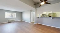 Located at 2880 W Ball Rd in Anaheim, California, this thoughtfully updated 2-bedroom, 1-bathroom residence offers a clean, modern aesthetic throughout its single-floor layout. Light wood flooring flows seamlessly through every room, creating a cohesive and airy feel. The open-concept living and kitchen area serves as the heart of the home, featuring a breakfast bar peninsula, white shaker cabinetry, stainless steel appliances — including a refrigerator, range, microwave, and dishwasher — and bright white countertops. A ceiling fan with integrated lighting anchors the living space, which benefits from natural light through a window and includes a wall-mounted AC unit for climate control. The primary bedroom is generously sized, offering a walk-in closet with dual hanging rods and ample storage. The second bedroom features a mirrored sliding-door closet, two windows for natural light, and its own ceiling fan. The bathroom is well-appointed with a wide vanity, white cabinetry, brushed gold fixtures, and a large wall mirror. Neutral gray walls, clean white trim, and consistent wood flooring throughout lend the space a polished, move-in-ready appeal.