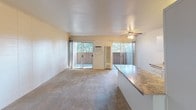 Located in Livermore, CA, this single-floor apartment at 3998 East Ave offers a practical and comfortable layout. The living area is open and spacious, featuring neutral carpeting, a ceiling fan with light fixture, and two sliding glass doors that flood the room with natural light and provide direct access to an outdoor patio area. Built-in shelving along one wall adds functional storage and display space, while the open connection to the kitchen creates an airy, connected feel.

The kitchen is laid out in a galley style, featuring white cabinetry above and below the counters, dark granite-style laminate countertops, a white electric range with overhead ventilation, and a white refrigerator. Tile flooring runs throughout the kitchen, and a walk-in pantry or storage closet is conveniently accessible from within the space.

The bathroom is clean and well-appointed, featuring a combination tub and shower enclosed by a frosted sliding glass door with chrome hardware. White tile surrounds the tub area, and a frosted privacy window above allows natural light to filter in. A grab bar and toilet complete the functional layout.

Overall, the unit presents a clean, move-in ready atmosphere with ample natural light, practical storage solutions, and easy indoor-outdoor flow.