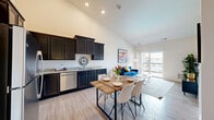 Located at 77 S Adams St in Oswego, Illinois, this single-floor, one-bedroom, one-bathroom residence offers a thoughtfully designed layout that maximizes its comfortable footprint. Soaring ceilings throughout create an airy, open atmosphere that amplifies the sense of space in every room.

The kitchen is a true standout, featuring rich dark cabinetry extending to ceiling height, light granite countertops, stainless steel appliances including a refrigerator, range, and microwave, and light wood-style flooring. The adjacent dining area provides a natural gathering space, completing a highly functional and visually striking culinary zone.

The bedroom is generously proportioned with soft wall-to-wall carpeting, a large window that invites natural light and neighborhood views, and direct access to a dedicated walk-in closet with a hanging rod for ample storage.

The bathroom maintains the same refined aesthetic found throughout the unit, showcasing granite-topped dark vanity cabinetry, a large mirror, light wood-style flooring, and clean, neutral wall tones that lend a calm, spa-like ambiance.

Neutral warm tones, consistent finishes, and tall ceilings tie the entire residence together into a cohesive, modern living experience in the heart of Oswego.