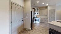 Located in Mooresville, NC, this well-appointed single-floor residence offers a thoughtfully designed open-concept layout that seamlessly connects the kitchen, dining, and living areas. The kitchen is a standout feature, equipped with stainless steel appliances including a side-by-side refrigerator with ice maker, an electric range, and an over-the-range microwave. Gray shaker-style cabinetry with frosted glass upper panels, a classic white subway tile backsplash, and a light stone countertop with an undermount sink complete the space. Pendant lighting and recessed fixtures illuminate the area effectively. The living room extends the open feel with luxury vinyl plank flooring, a ceiling fan, and French doors that lead to a private balcony with outdoor views. Bedrooms feature plush carpeting, ceiling fans, and ample natural light from well-placed windows. The primary bedroom includes an en-suite bathroom with a soaking tub, a separate glass-enclosed shower, and subway tile surround. A secondary full bathroom offers a shower/tub combination with overhead cabinetry. Neutral warm-toned walls and consistent gray trim details throughout contribute to a cohesive, modern aesthetic across the entire residence.