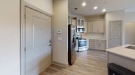 Located in Mooresville, NC, this well-appointed single-floor residence offers a thoughtfully designed open-concept layout that seamlessly connects the kitchen, dining, and living areas. The kitchen is a standout feature, equipped with stainless steel appliances including a side-by-side refrigerator with ice maker, an electric range, and an over-the-range microwave. Gray shaker-style cabinetry with frosted glass upper panels, a classic white subway tile backsplash, and a light stone countertop with an undermount sink complete the space. Pendant lighting and recessed fixtures illuminate the area effectively. The living room extends the open feel with luxury vinyl plank flooring, a ceiling fan, and French doors that lead to a private balcony with outdoor views. Bedrooms feature plush carpeting, ceiling fans, and ample natural light from well-placed windows. The primary bedroom includes an en-suite bathroom with a soaking tub, a separate glass-enclosed shower, and subway tile surround. A secondary full bathroom offers a shower/tub combination with overhead cabinetry. Neutral warm-toned walls and consistent gray trim details throughout contribute to a cohesive, modern aesthetic across the entire residence.