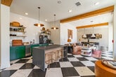 Located at 9166 Crestline Lane in Collierville, Tennessee, this thoughtfully designed single-floor amenity space offers a versatile and visually striking environment for both socializing and productivity. The interior is immediately defined by bold black-and-white checkered tile flooring that flows throughout the main areas, complemented by exposed wood ceiling beams that add warmth and architectural character.

The open-concept lounge and social area is bathed in natural light from large sliding glass doors and floor-to-ceiling windows, offering views of the surrounding community. Comfortable and eclectic seating arrangements — including curved lounge chairs in rich cognac leather, a tufted round ottoman, and plush sofas — create an inviting atmosphere for gathering and relaxation.

A well-appointed kitchenette features bold green cabinetry, subway tile backsplash, open brass shelving, a stone-topped island with bar seating, and a coffee station, making it ideal for casual refreshments. A dedicated dining area with a long wooden table and upholstered chairs sits beneath a statement cone pendant light.

For focused work, the space includes a private conference room with deep green walls, a round table, executive seating, and a wall-mounted display screen, as well as a quiet individual work nook fitted with a built-in desk, decorative wallpaper, and ambient sconce lighting.