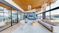 Located at 2821 Pheasant Hollow Dr in Plainsboro, NJ, this thoughtfully designed amenity space delivers a seamless blend of comfort, functionality, and contemporary style across a single well-appointed floor. The centerpiece is a spacious lounge area distinguished by soaring vaulted ceilings clad in warm natural wood, dramatic floor-to-ceiling glass walls that flood the interior with abundant natural light, and sweeping views of the surrounding greenery. A bold navy blue shiplap feature wall anchors the lounge, complemented by a wall-mounted TV, elegant pendant lighting, and a curated arrangement of neutral-toned sofas and accent chairs atop a patterned area rug. Light hardwood flooring flows throughout the common areas, reinforcing the space's bright, airy character. Two private offices, accessible via sleek glass-panel partitions with black steel frames, offer a quiet and productive environment furnished with natural wood desks, modern task chairs, and tasteful abstract artwork. The fitness center is generously sized and well-equipped with treadmills, ellipticals, and a variety of strength and cardio machines, all beneath the same striking wood-beam ceiling and framed by large windows overlooking the outdoor area. Navy cabinetry provides organized storage, while mirrored walls enhance the sense of openness throughout this exceptional amenity space.
