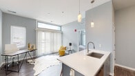 Located at 3420 Broadway Blvd in Kansas City, Missouri, this modern single-floor residence offers a thoughtfully designed open-concept layout with clean contemporary finishes throughout. The living area is bathed in natural light courtesy of large floor-to-ceiling windows fitted with vertical blinds, creating a bright and airy atmosphere against soft gray walls and durable wood-look flooring that extends seamlessly through the space.

The kitchen is efficiently appointed with stainless steel appliances — including a full-size refrigerator, range, and microwave — complemented by sleek gray cabinetry, white quartz countertops, and an undermount sink. A peninsula with pendant lighting provides additional prep space and casual seating, connecting the kitchen to the main living area.

A flexible secondary room, suitable as a bedroom or home office, features wall sconces, wood-look flooring, and generous window exposure that fills the space with natural light. The bathroom is finished with wood-grain tile flooring, a modern gray vanity with an integrated sink, and a tiled walk-in shower. A smart thermostat adds a layer of modern convenience to the unit. Overall, the space presents a cohesive, contemporary aesthetic well-suited for comfortable urban living in Kansas City.