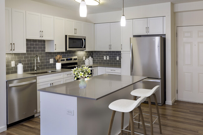 Renovated Package II kitchen with grey quartz countertops, white shaker cabinetry, stainless steel appliances, grey tile backsplash, and hard surface flooring throughout - Avalon Natick