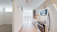 Located at 11500 Commerce Park Dr in Reston, VA, this single-floor unit offers a clean, modern design with an open and airy layout. Light hardwood flooring flows seamlessly throughout the main living areas, complementing the bright white walls and creating a cohesive, contemporary aesthetic.

The kitchen is a standout feature, equipped with stainless steel appliances including a range, over-the-range microwave, dishwasher, and refrigerator. Light wood cabinetry with sleek hardware pairs elegantly with a geometric mosaic tile backsplash and a undermount sink. Track lighting overhead provides focused illumination across the workspace.

The open living area benefits from an abundance of natural light streaming through large floor-to-ceiling windows fitted with horizontal blinds, offering both brightness and privacy. The spacious layout provides generous room for a variety of furniture configurations.

The bathroom is finished in a clean, minimalist style, featuring large-format white subway tile surrounding a soaking tub and shower combination, light tile flooring, and warm wood cabinetry above. A marble-style countertop adds a refined touch.

Additional hallway space connects the rooms efficiently, with continued hardwood flooring and track lighting maintaining a consistent design language throughout the unit. Overall, the space presents a polished, move-in-ready environment well-suited for modern living.