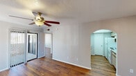 This single-floor residence offers a cohesive and functional layout highlighted by rich hardwood flooring that flows consistently throughout every room. The living area is generously sized, featuring a ceiling fan with light fixture and a sliding glass door that connects to an outdoor patio, allowing natural light to fill the space. A distinctive arched doorway serves as an elegant transition from the living and dining area into the galley-style kitchen, adding a classic architectural touch. The kitchen is efficiently designed with ample upper and lower cabinetry trimmed in warm wood tones, light countertops, a double stainless steel sink, a full-size refrigerator, and an electric range — all complemented by a skylight panel overhead that brightens the workspace. A dedicated bedroom features a sun-catching arched window that frames outdoor views, adding character and warmth to the room. Additional rooms include a space with accordion-style closet doors providing convenient storage. The bathroom is well-appointed with a wide vanity, an extended mirror with strip lighting above, and generous under-sink cabinetry. Textured ceilings are present throughout, and neutral gray-toned walls create a clean, move-in-ready backdrop. The overall layout is practical, well-connected, and comfortable.
