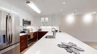 This 1-bedroom, 1-bathroom residence is thoughtfully designed with a clean, modern aesthetic that maximizes both function and style. The kitchen serves as a standout feature, showcasing a striking two-tone design with rich, dark wood lower cabinets paired against crisp white upper cabinetry — some with glass-front doors for an open, airy feel. The generous white countertop provides ample prep space and extends to form an island-style surface, making it ideal for cooking and casual dining. Stainless steel appliances, including a range with oven and an over-the-range microwave, add a professional touch to the culinary space. A deep undermount sink with a contemporary arc faucet anchors the layout, while recessed and flush-mount lighting illuminates the space with a bright, welcoming glow. The light-toned flooring complements the white walls and cabinetry, creating a cohesive and airy atmosphere throughout. The overall design balances practicality with modern elegance, offering a comfortable and visually appealing living environment well-suited for everyday living.