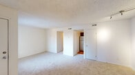 Located at 8237 S Yorktown Ave in Tulsa, Oklahoma, this single-floor unit offers a practical and well-organized layout across a compact footprint. The spacious living room is finished with neutral wall-to-wall carpeting and features a textured ceiling, recessed HVAC vents, and a large window that invites natural light, creating a bright and open atmosphere. The floor plan flows seamlessly through a connecting hallway into the kitchen area, which includes warm wood-toned cabinetry and a marble-patterned countertop, complemented by hardwood-style flooring that transitions from the carpeted living spaces. A stainless steel refrigerator anchors the kitchen, providing a modern touch alongside the classic cabinetry. The bathroom is clean and functional, featuring hardwood-style flooring, a white vanity with a basin sink, a toilet, and chrome towel bars, all framed by crisp white walls. A hallway connects the rooms efficiently, reinforcing the unit's straightforward and accessible layout. Throughout the space, the consistent use of white and neutral tones, combined with natural light from the windows, lends a clean, airy feel well-suited for practical, comfortable everyday living.