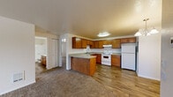 Located at 8530 Fifth Ave W in Everett, Washington, this single-floor, 2-bedroom, 1-bathroom home offers a functional and comfortable layout. The open-concept kitchen and living area serves as the heart of the home, with warm wood-toned cabinetry, ample upper and lower storage, a peninsula with countertop seating, and white appliances including a range, refrigerator, and dishwasher. Durable wood-look flooring runs throughout the kitchen, while plush carpet extends into the living areas and bedrooms. The living room is a standout space, featuring a classic white brick fireplace and a sliding glass door that opens to a private wooden deck overlooking a serene, tree-lined outdoor setting. Both bedrooms are carpeted and well-proportioned, with the primary bedroom offering a window with views of mature trees and a dedicated closet. The second bedroom includes a sliding closet and access to the hallway. The full bathroom is neatly appointed with wood-look flooring, a single-sink vanity with granite-style countertop, a large mirror, and a shower-tub combination. Two closets provide practical storage throughout the home. Textured ceilings and neutral wall tones lend a clean, cohesive feel to the entire space.