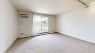 This studio unit at 1414 Third St S in Minneapolis, MN offers a practical and efficient single-floor layout. The open living area is finished with neutral carpet and light tile flooring, creating a clean, cohesive aesthetic throughout. A wall-mounted air conditioning unit and baseboard heating ensure year-round comfort, while a sliding glass door fills the space with natural light and opens to a private balcony overlooking the surrounding cityscape.

The kitchenette is thoughtfully equipped with warm-toned wood cabinetry featuring glass-front upper doors, a single-basin sink, an electric range, and a full-size refrigerator. Track lighting overhead provides focused illumination across the cooking area. The transition between the tiled kitchen zone and the carpeted living space creates a natural delineation within the open floor plan.

A dedicated entrance area includes a walk-in closet with wire shelving, offering valuable storage in a compact footprint. The full bathroom is finished with classic mosaic tile flooring and includes a vanity, toilet, and a shower-tub combination with a curtain. A textured ceiling adds a subtle architectural detail throughout the unit. Overall, the studio presents a straightforward, functional layout well-suited for efficient urban living in the heart of Minneapolis.