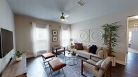 This single-floor residence offers a thoughtfully designed layout that balances modern finishes with a warm, neutral aesthetic throughout. Dark hardwood-style flooring flows through the main living areas and hallway, creating a cohesive and polished foundation.

The kitchen is a standout space, featuring rich dark cabinetry extending to the ceiling, crisp white countertops, a textured tile backsplash, and a full suite of stainless steel appliances, including a range, microwave, dishwasher, and refrigerator. Adjacent to the kitchen, the dining area accommodates a glass-top table beneath a multi-shade chrome chandelier, adding a contemporary touch.

The living room is bright and welcoming, with multiple windows dressed in sheer white curtains, a ceiling fan with a light fixture, and decorative wall art panels. The bedroom features plush carpeting, multiple windows with blinds and curtain rods, a ceiling fan, and direct access to an outdoor area via a glass door. The full bathroom includes a tub-shower combination, a dark vanity with a white countertop, and tall ceilings. Completing the unit is a dedicated laundry room with a full-size washer and dryer.